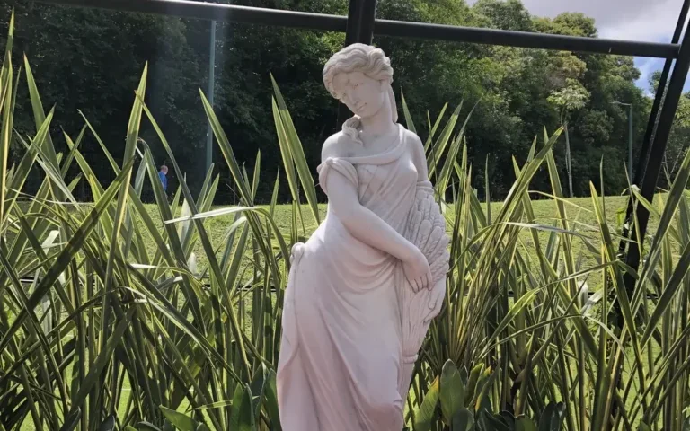 Estátua de uma mulher em mármore entre folhagens altas de um jardim